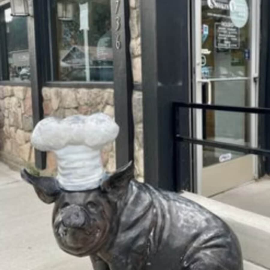A bronze statue of a pig wearing a chef's hat stands outside a restaurant.