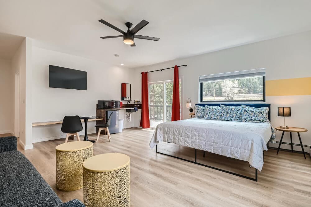 Cozy studio apartment featuring a bed, kitchenette, seating area, and large window with natural light.