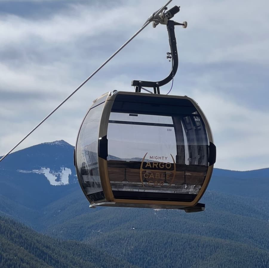 A clear cable car hangs over a mountainous landscape under a cloudy sky.